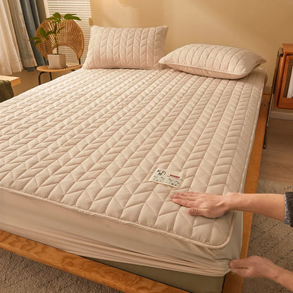 Beige quilted mattress cover on a bed with a hand adjusting it, in a bedroom setting.
