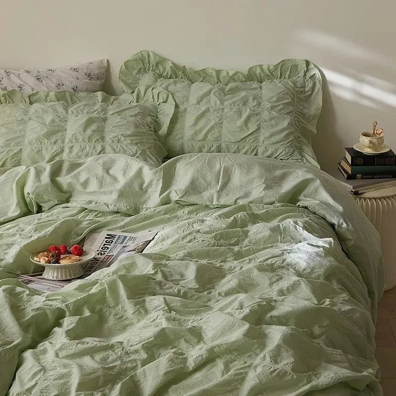 Green bedspread on a bed with a side table and books in the background
