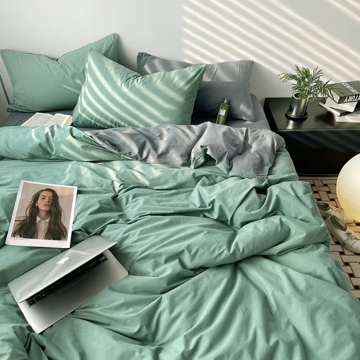 Bed with teal bedding and pillows, laptop, and photo on a nightstand.