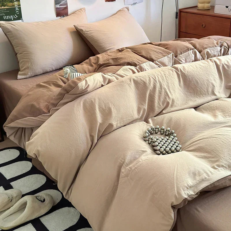 Beige comforter set on a bed with pillows and slippers in the foreground.