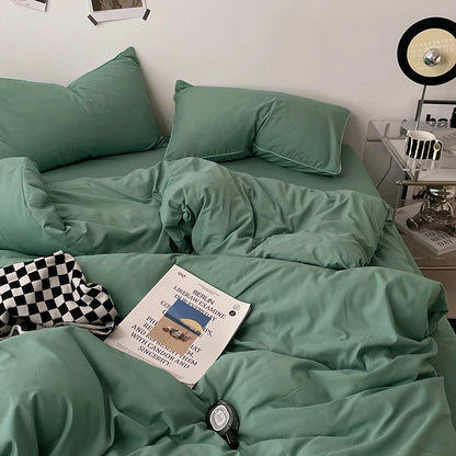 Green bedspread on a bed with a magazine and watch on top, nightstand with lamp in the background