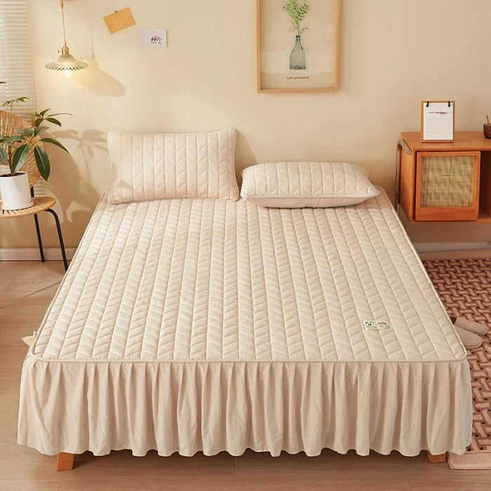 Beige quilted mattress cover on a bed in a bedroom setting.