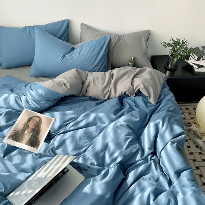 Bed with blue and gray bedding, laptop, and books on a nightstand.