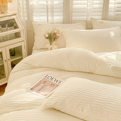 Neatly made bed with white bedding and pillows, LOEWE magazine on the bed, and a side table with decorative items.