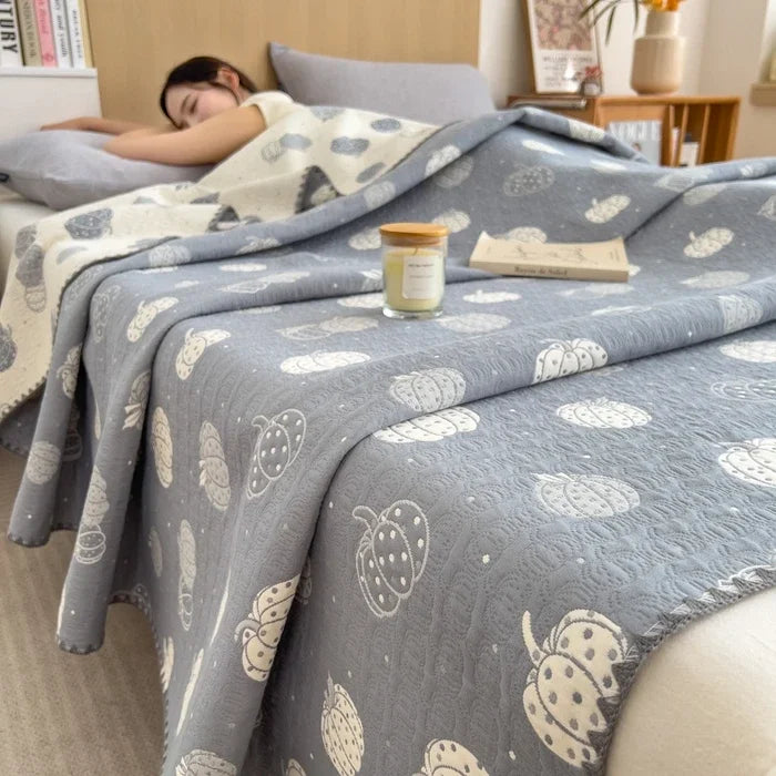 Person sleeping under a patterned gray blanket with a candle and book on a bed.