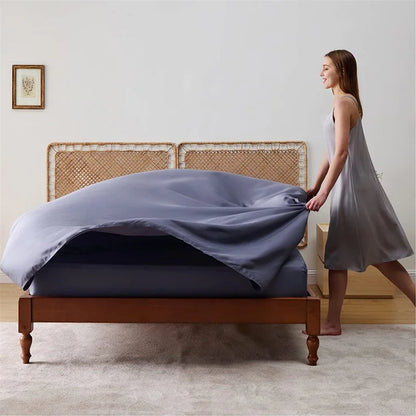 Woman in a light dress adjusting a fitted sheet on a wooden bed in a room with a white wall and framed picture.