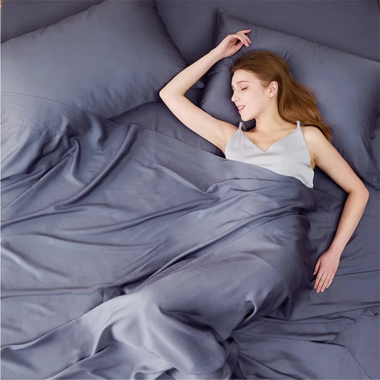 Woman lying in bed under gray bedding with a pillow behind her head.
