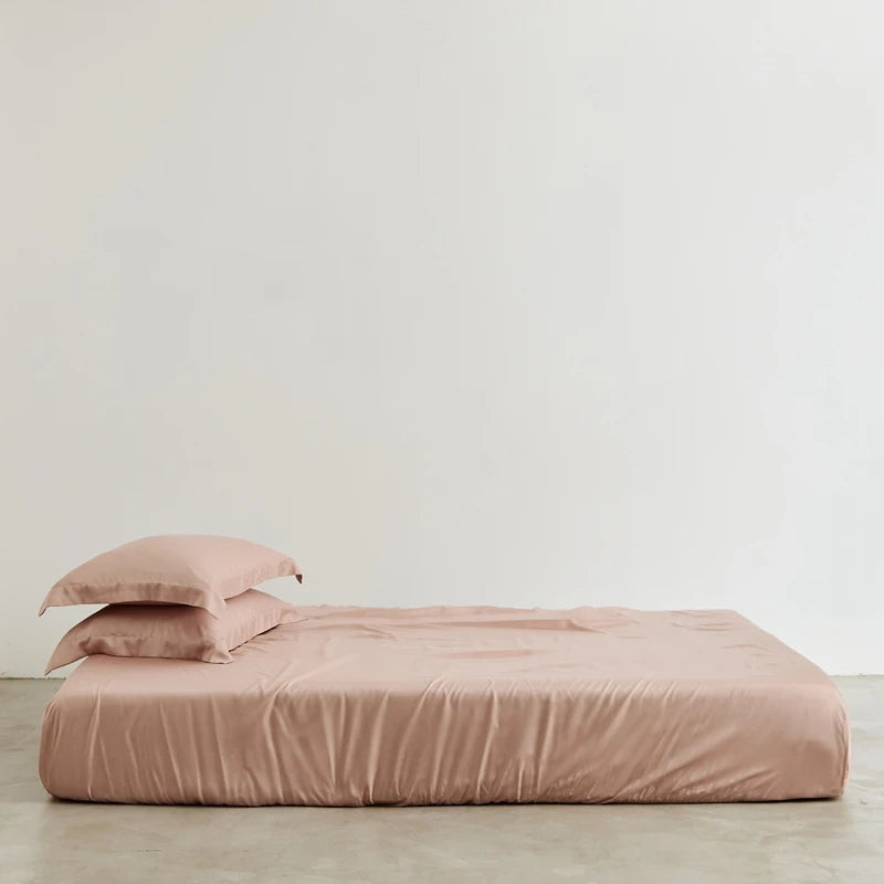 Pink bedspread and pillow on a bed against a plain wall