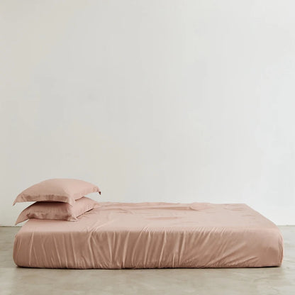 Pink bedspread and pillow on a bed against a plain wall