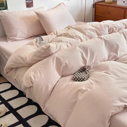 Pink comforter on a bed with pillows and a side table in the background