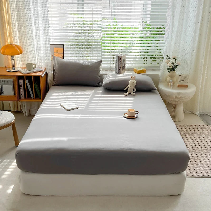 Bed with gray mattress cover in a bright room with windows and furniture.