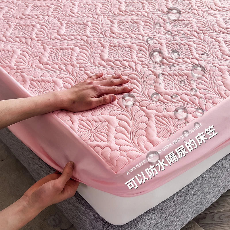 Pink quilted mattress cover with water droplets and a hand touching it, on a wooden floor.