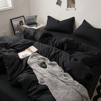 Bed with black bedding and a gray blanket, with a laptop and magazines on a nightstand.