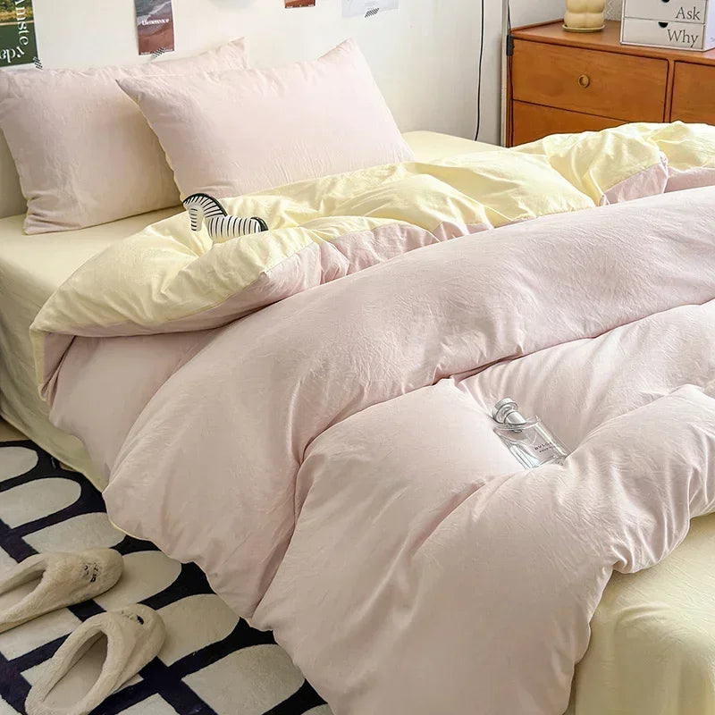 Pink comforter on a bed with pillows and slippers on the floor.