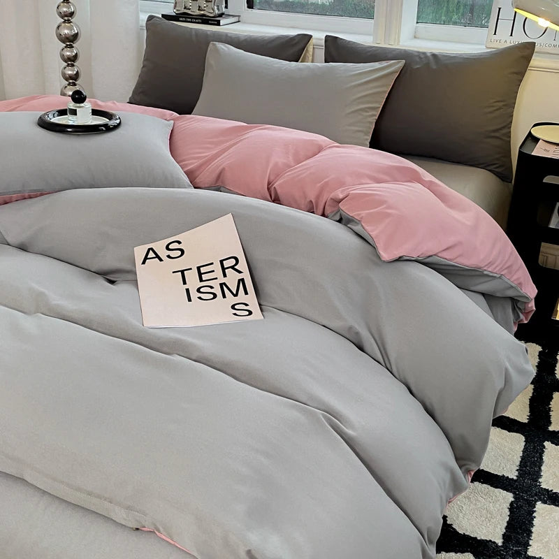 Gray and pink bedding set on a bed with a book titled 'Asterisms' on top.