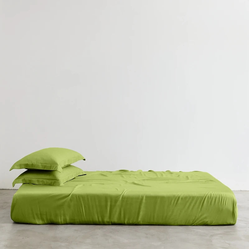 Green bed sheets and pillowcases on a bed against a white wall.