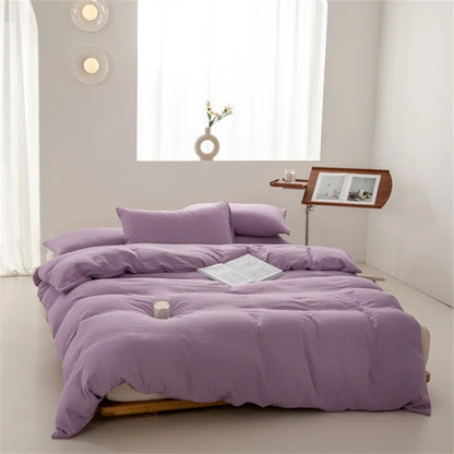 Purple bedding set on a bed in a minimalistic room with a window and side table.
