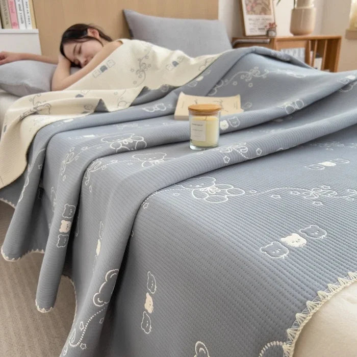 Person sleeping under a patterned gray blanket with a candle on a nightstand.