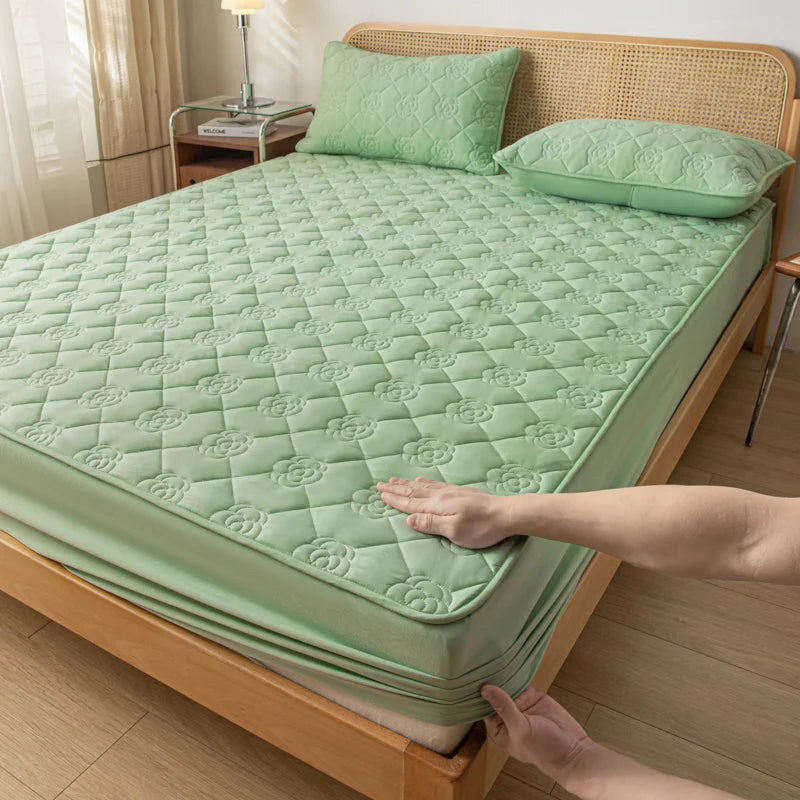 Green quilted mattress cover on a wooden bed with a hand touching it.
