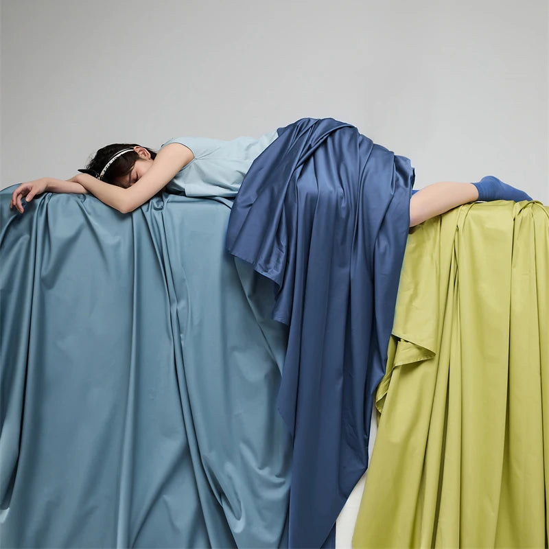 Person lying on draped fabric in blue and green with a neutral background