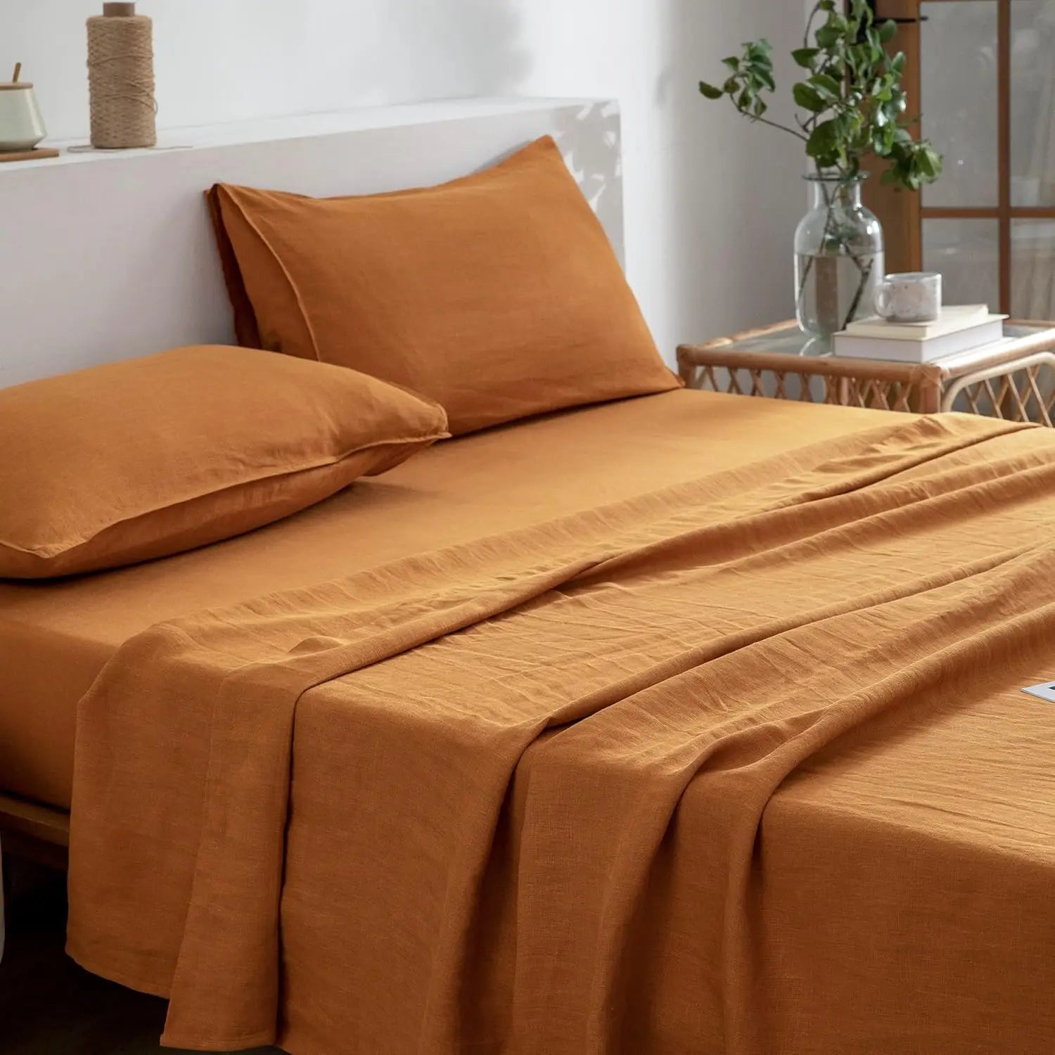 Orange bedspread and pillows on a bed with a side table in the background.