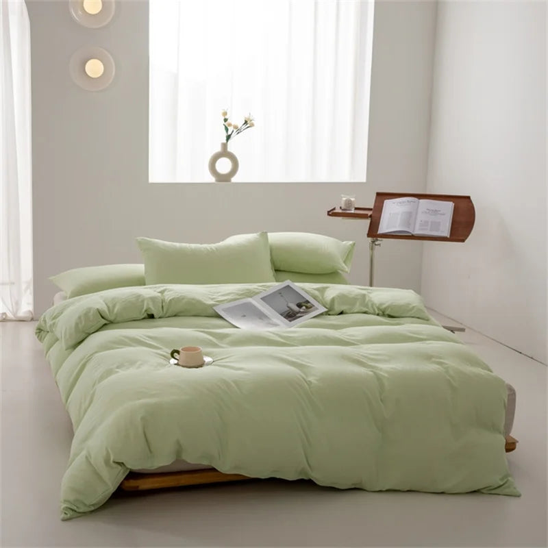 Light green bedding set on a bed in a bright room with a small table and lamp.