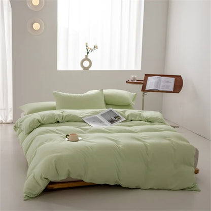 Light green bedding set on a bed in a bright room with a small table and lamp.