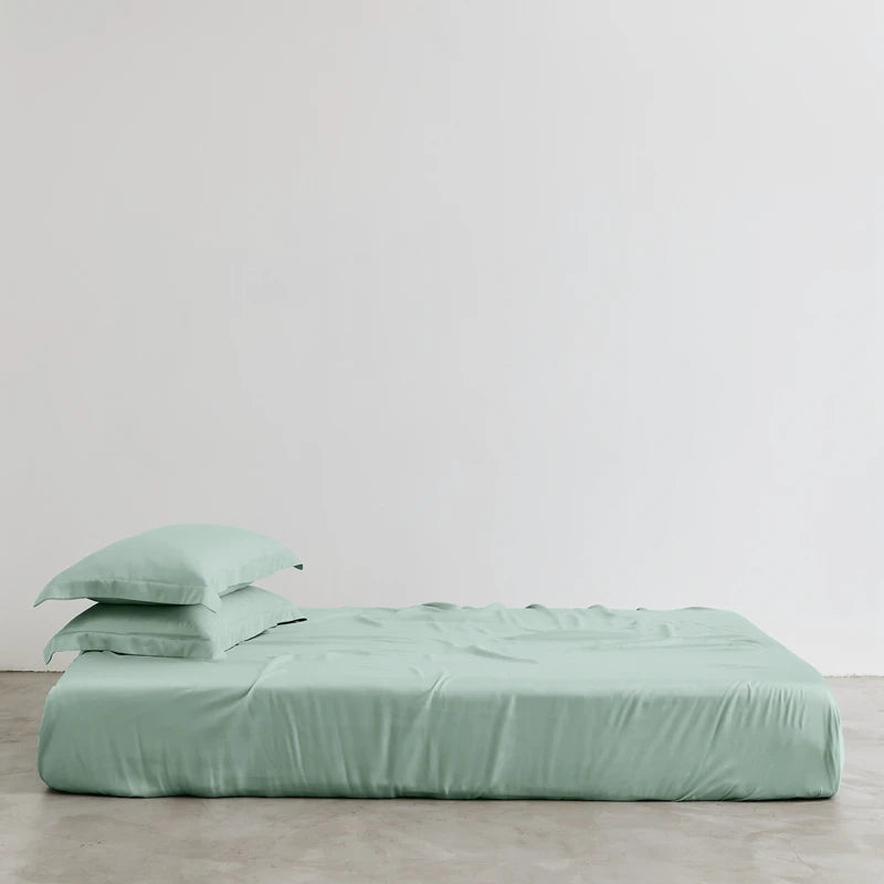 Green bed sheets and pillowcases on a bed against a plain background