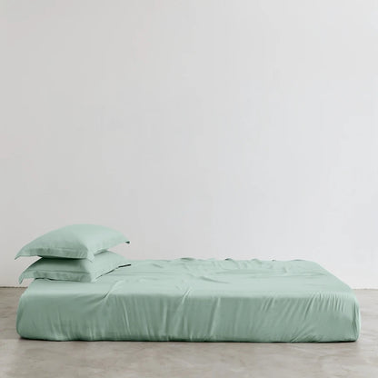 Green bed sheets and pillowcases on a bed against a plain background