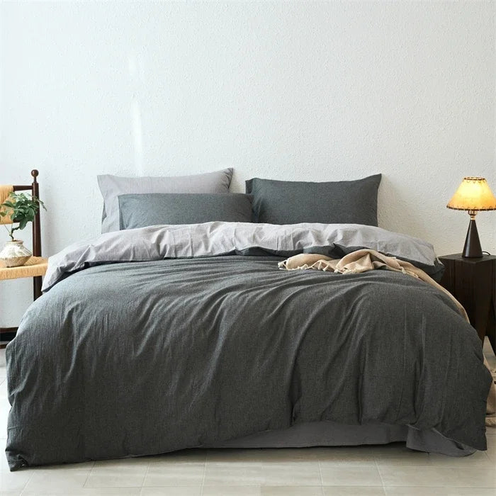 Gray bedding set on a bed in a minimalistic bedroom with a lamp and plant.
