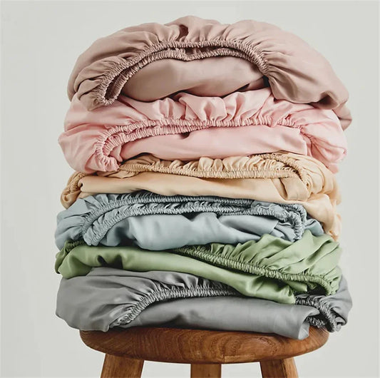 Stack of colorful fitted sheets on a wooden stool against a light background