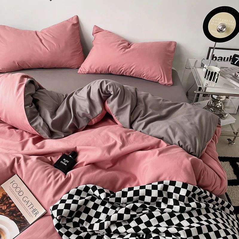 Pink and gray bedding set on a bed with a checkered blanket, in a room setting.