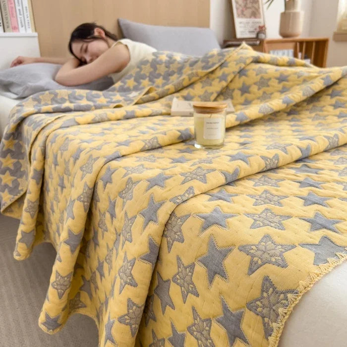Yellow blanket with star pattern draped over a bed, with a person partially visible underneath.