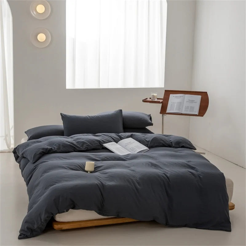 Gray bedding set on a bed in a minimalistic room with a window and side table.