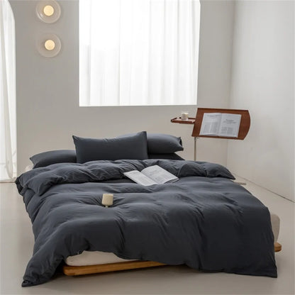 Gray bedding set on a bed in a minimalistic room with a window and side table.