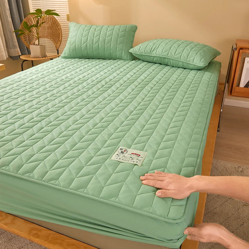 Green quilted mattress cover on a bed with a hand touching it, in a room setting.