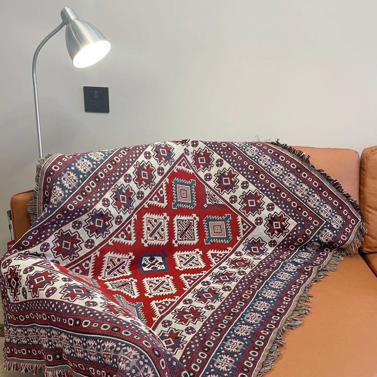 Decorative patterned blanket draped over a couch with a lamp in the background.