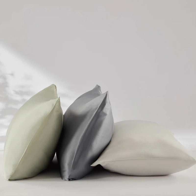 Three pillows in light green, gray, and white on a light gray background