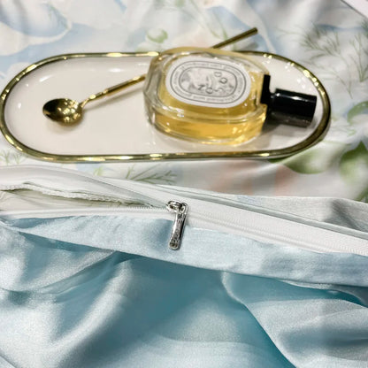 Perfume bottle on a white floral surface with a silver clutch.
