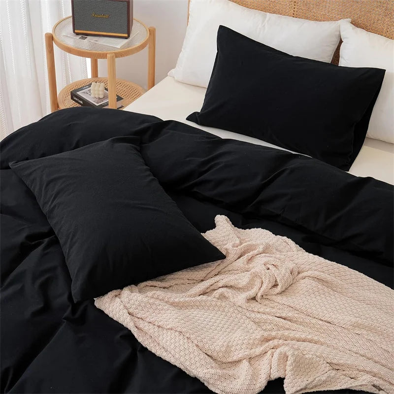 Black bedding set on a bed with a beige blanket and side table in the background.