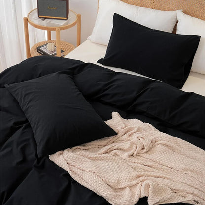 Black bedding set on a bed with a beige blanket and side table in the background.
