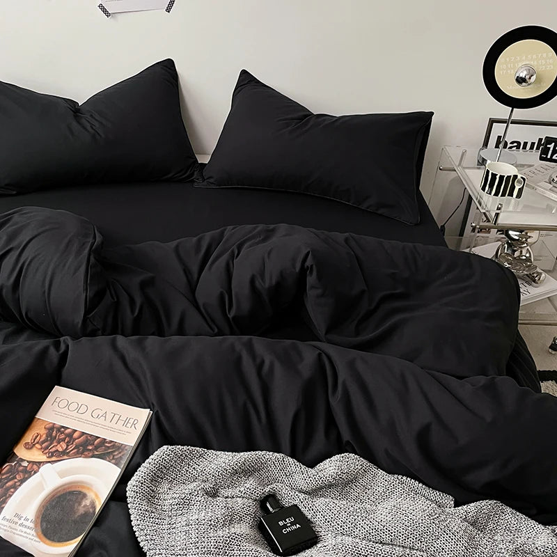 Black bedding set on a bed with a side table and decor items in the background.