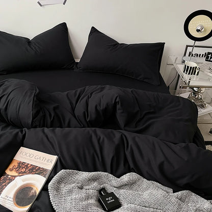 Black bedding set on a bed with a side table and decor items in the background.