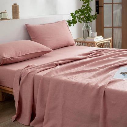 Pink bedding set on a bed with a side table and plant in the background.