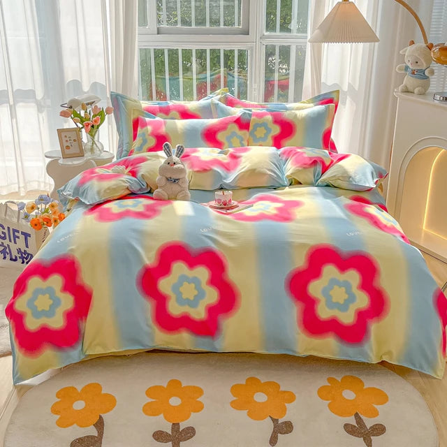 Colorful floral bedspread on a bed in a bright room with flowers and toys on the nightstand.