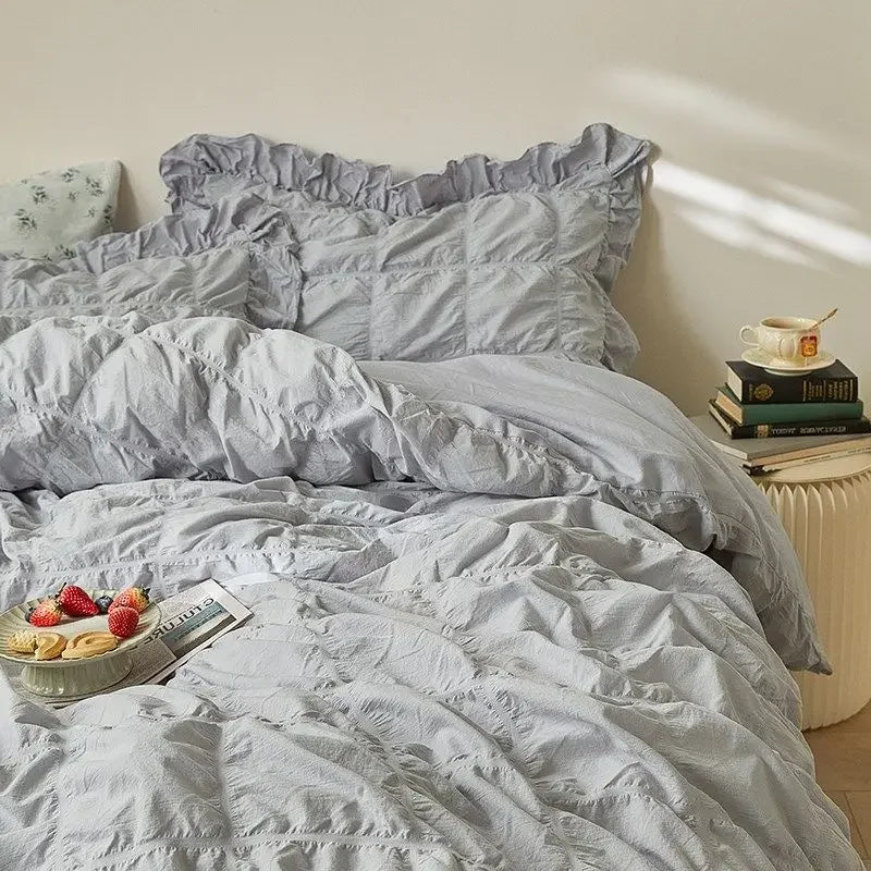 Light gray bedding set on a bed with a side table and books in the background.