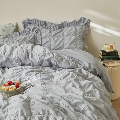 Light gray bedding set on a bed with a side table and books in the background.