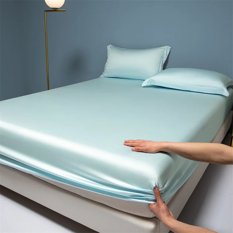Light blue satin sheet set on a bed with a person's hand touching it.