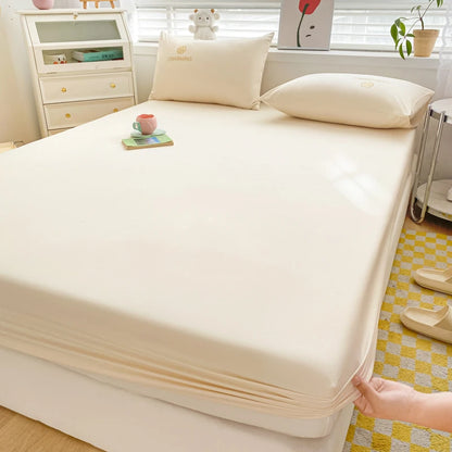 Beige mattress cover being fitted onto a bed in a bedroom setting.
