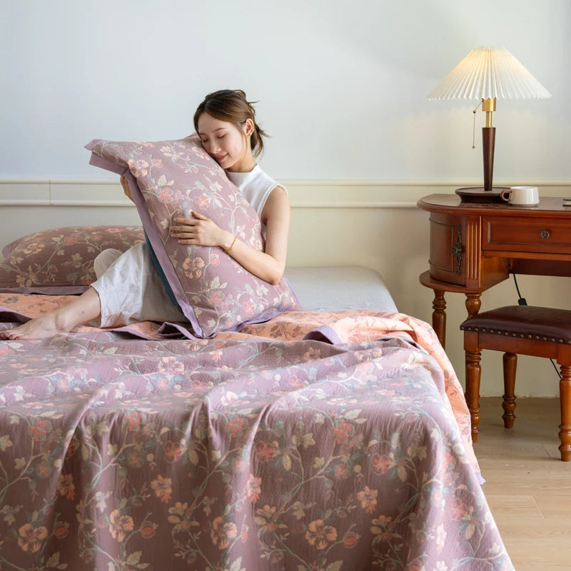 Woman sitting on a bed with floral bedding and pillow, in a room with wooden furniture.